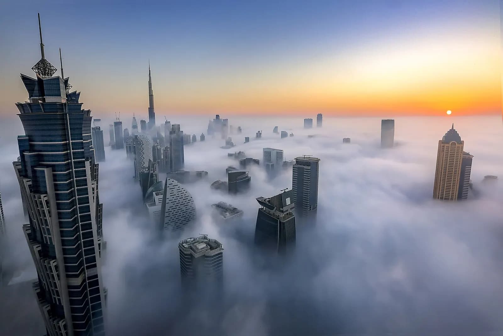 Dubai towers rising above early morning fog at sunrise, with the Burj Khalifa in the distance