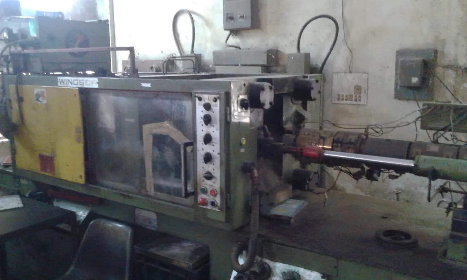 Older injection moulding machine with a long barrel and control cabinet in a workshop