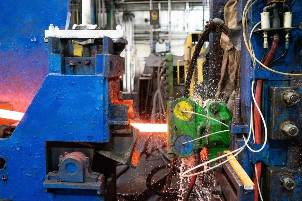 Close view of a steel mill rolling stand with blue machinery, cables and hot metal