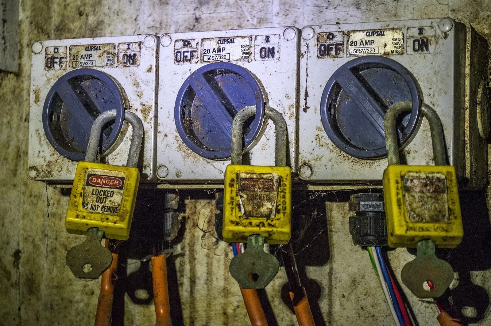 Three rotary isolators switched off and secured with yellow safety padlocks, one carrying a danger tag