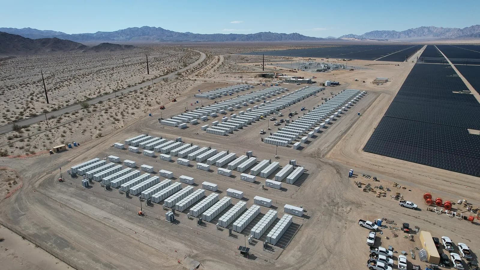 Aerial view of a desert solar farm with rows of battery storage containers beside the panel field