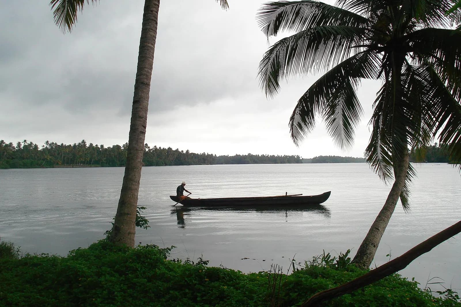 Kerala backwater under heavy monsoon clouds with a fisherman's canoe and coconut palms