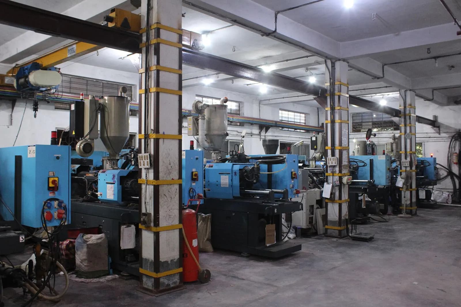 Long factory hall with green process machines, overhead ducting and a forklift in the aisle