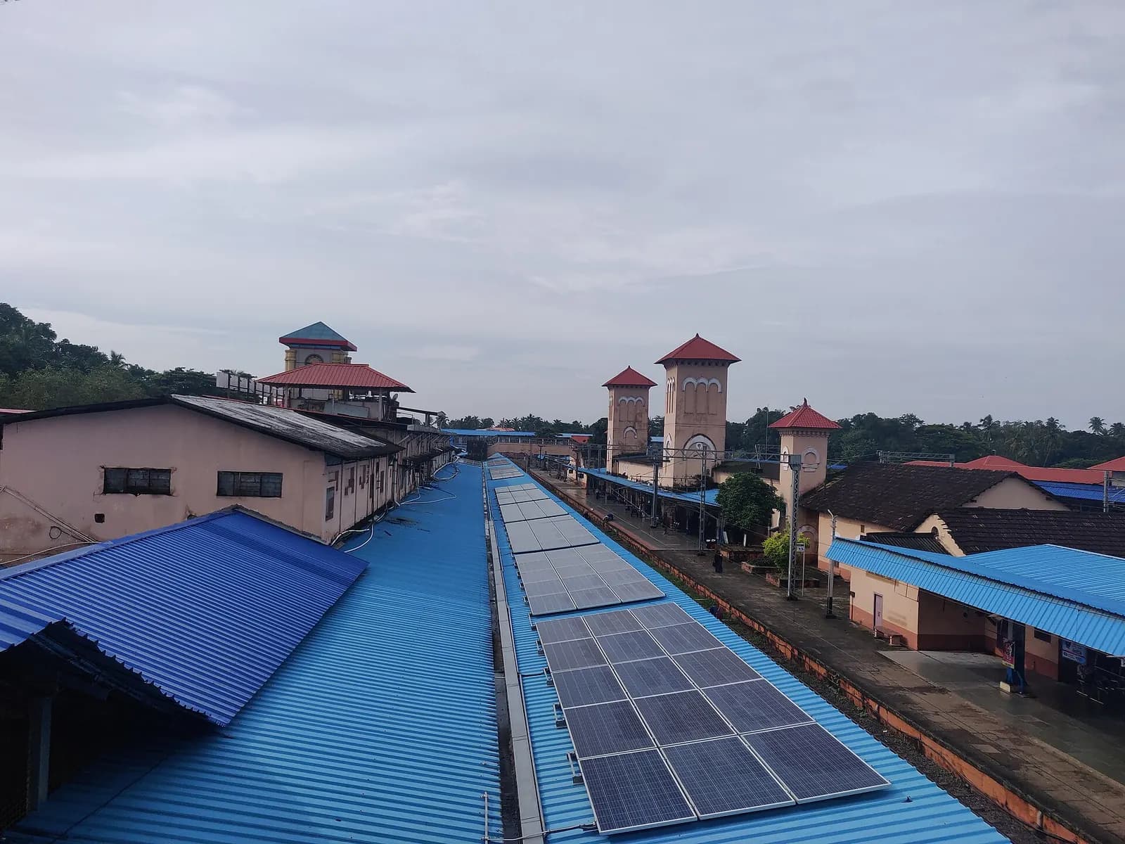 Rows of solar panels on the blue roofs of Kozhikode railway station under a cloudy sky