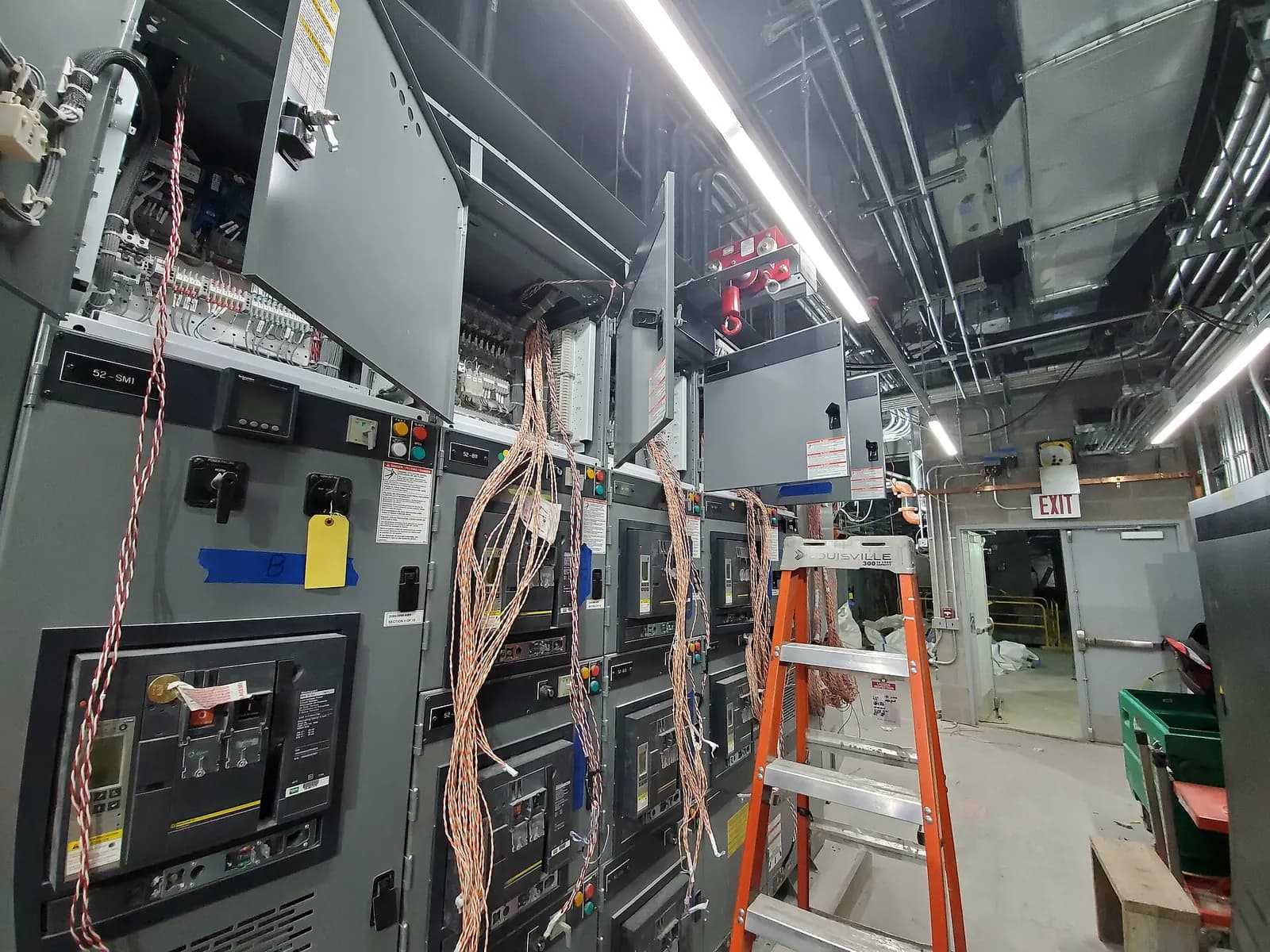 Switchgear and control panels with doors open and temporary test wiring connected during system testing in an electrical room