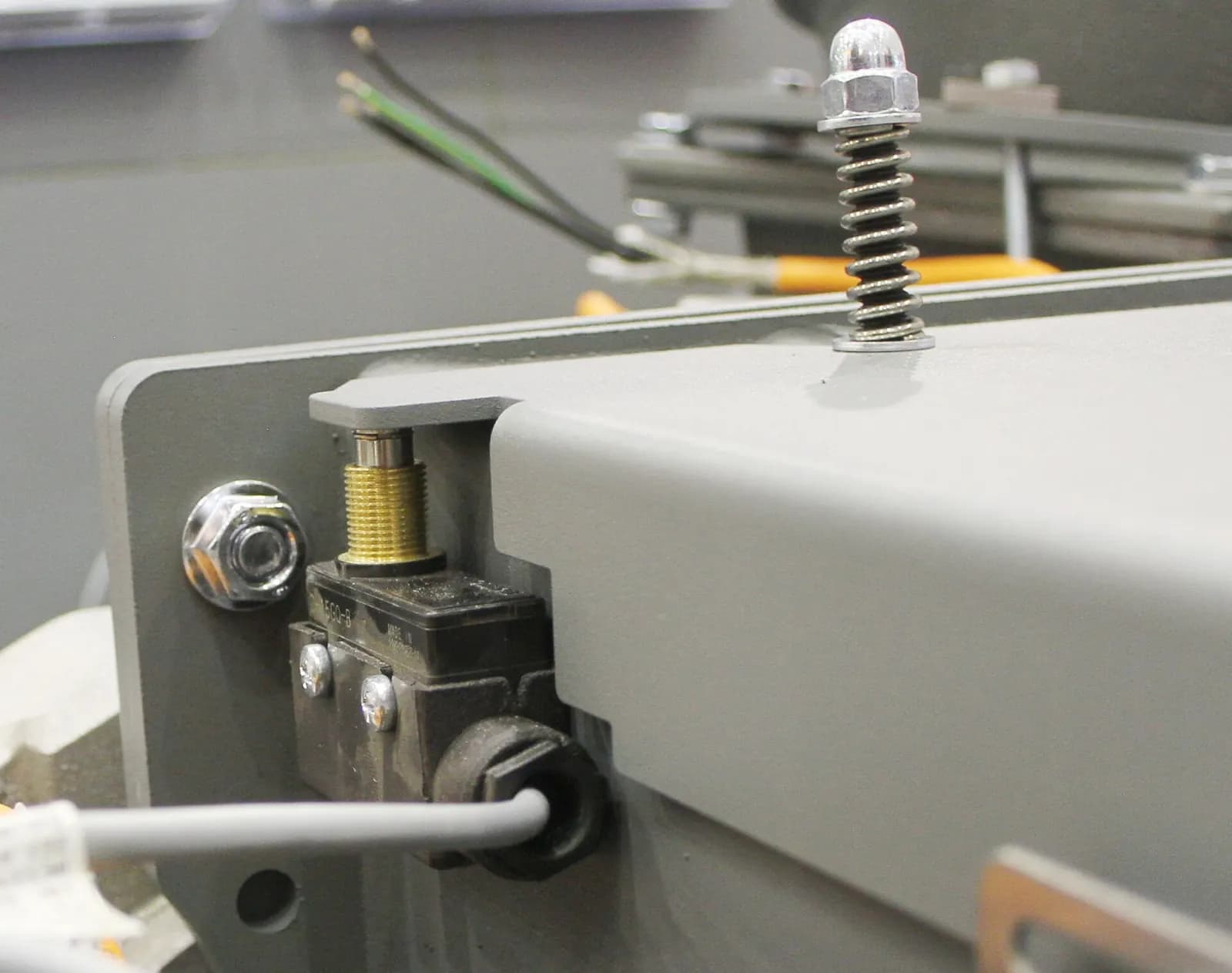 Limit switch with a brass plunger mounted on the grey steel flap of a machine, with its cable running out of the housing