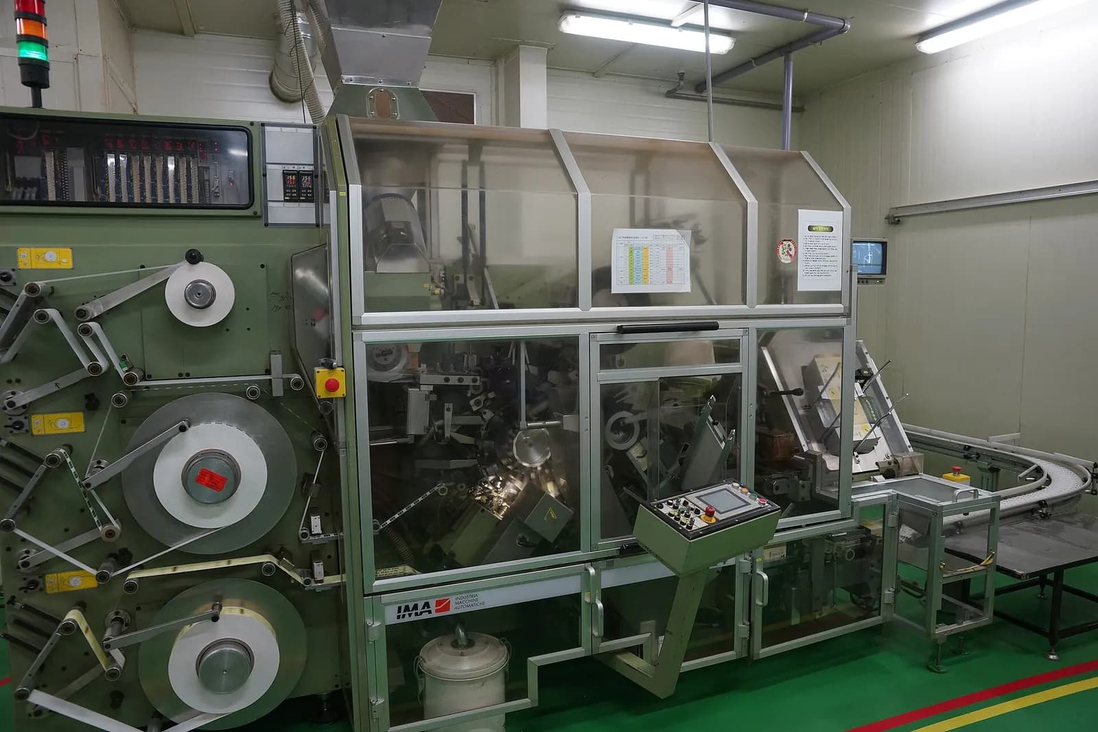 Enclosed packaging machine with guarded film rolls, a touch panel and a signal tower in a clean production room