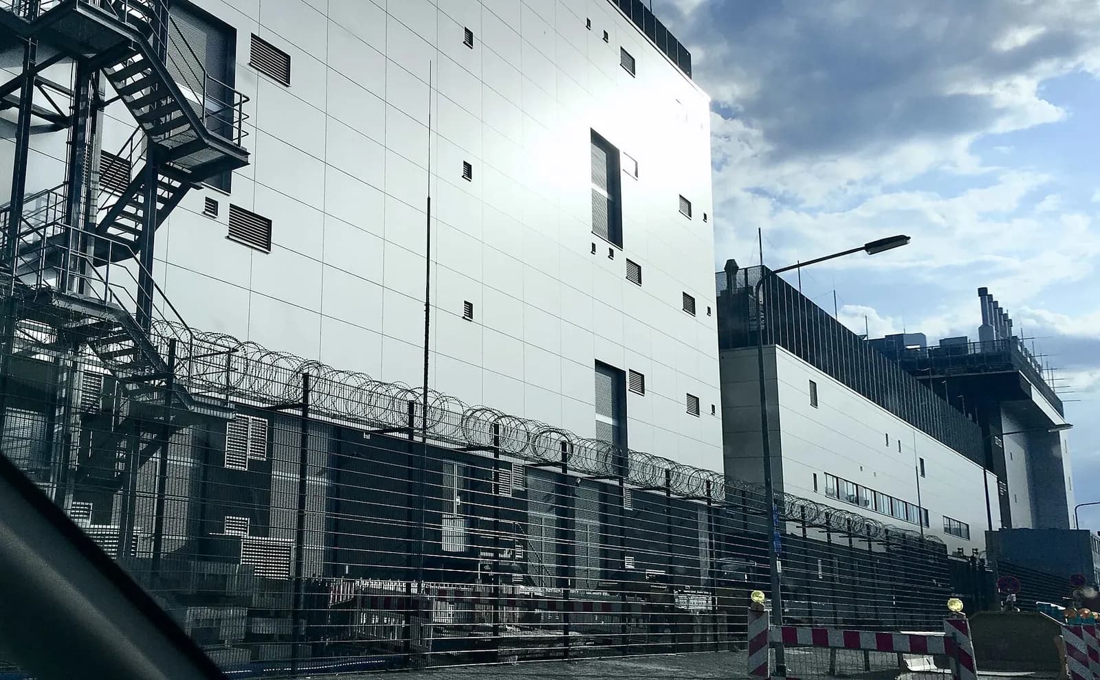 Data centre building behind a steel security fence topped with barbed wire, with an external fire escape