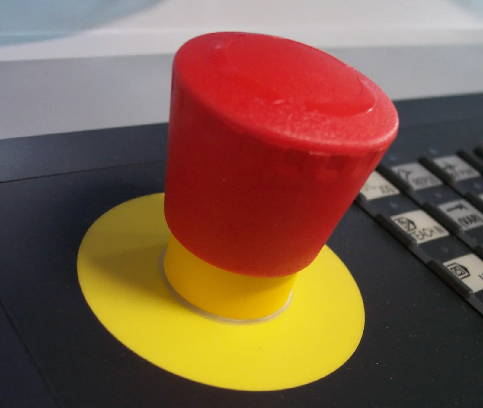 Red emergency off push button on a yellow collar mounted on a grey machine control surface