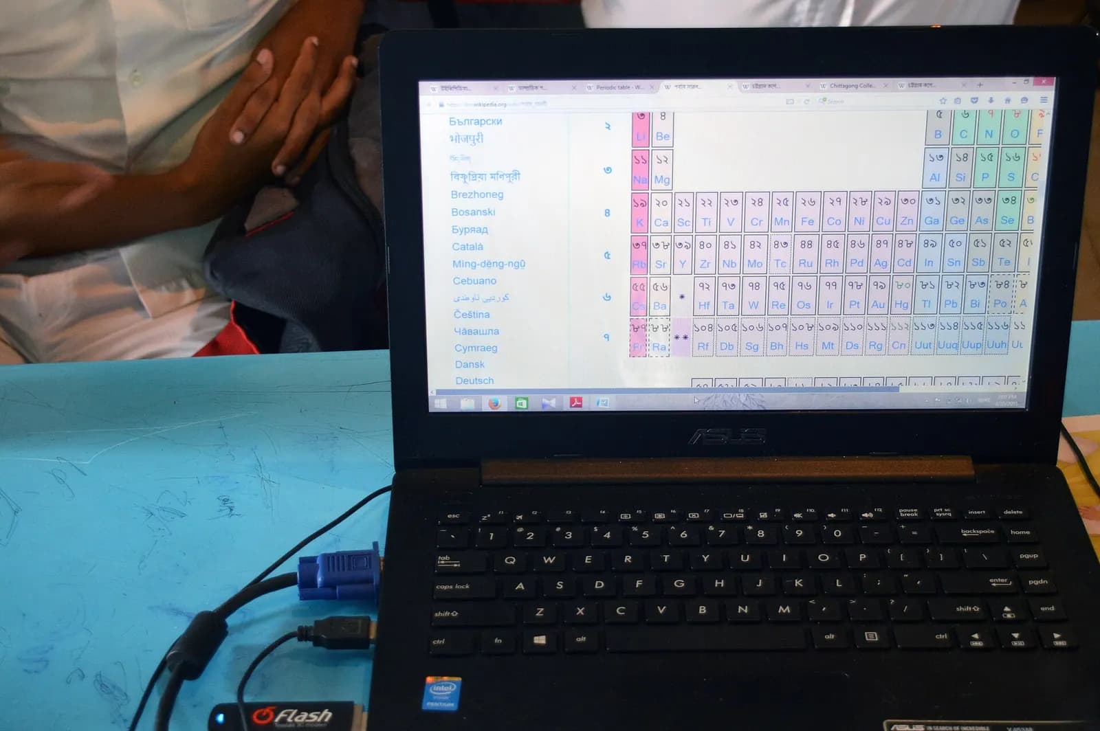 Laptop on a blue classroom desk with a browser open and a USB modem plugged in