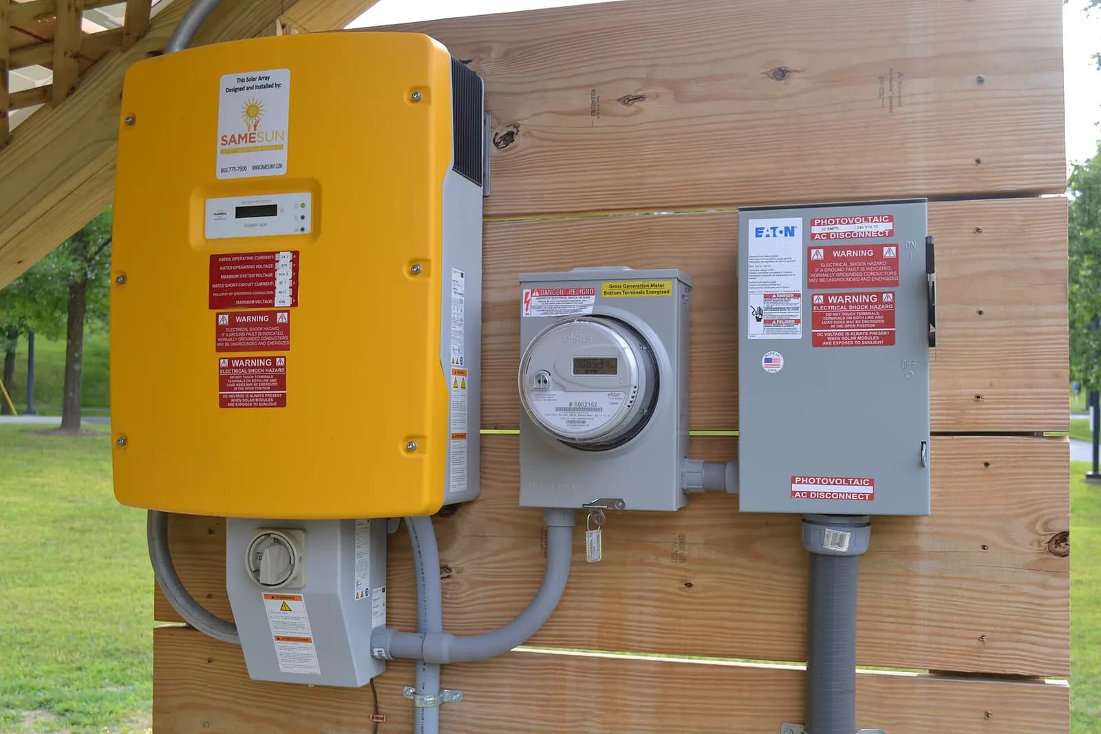 Yellow grid-tie solar inverter mounted on a wooden wall beside an electricity meter and isolator switches