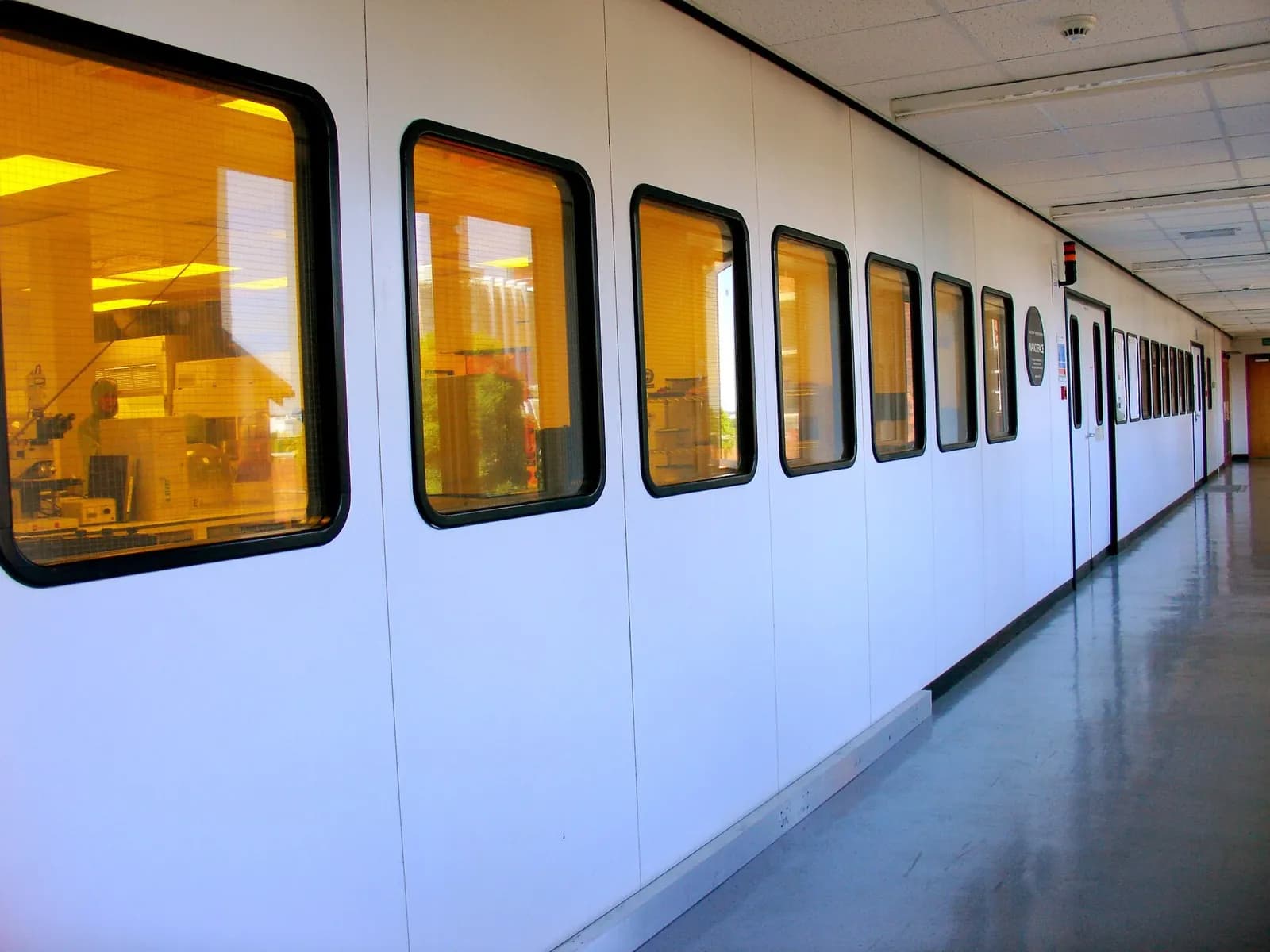 Exterior of a cleanroom suite seen from a white corridor with a row of observation windows