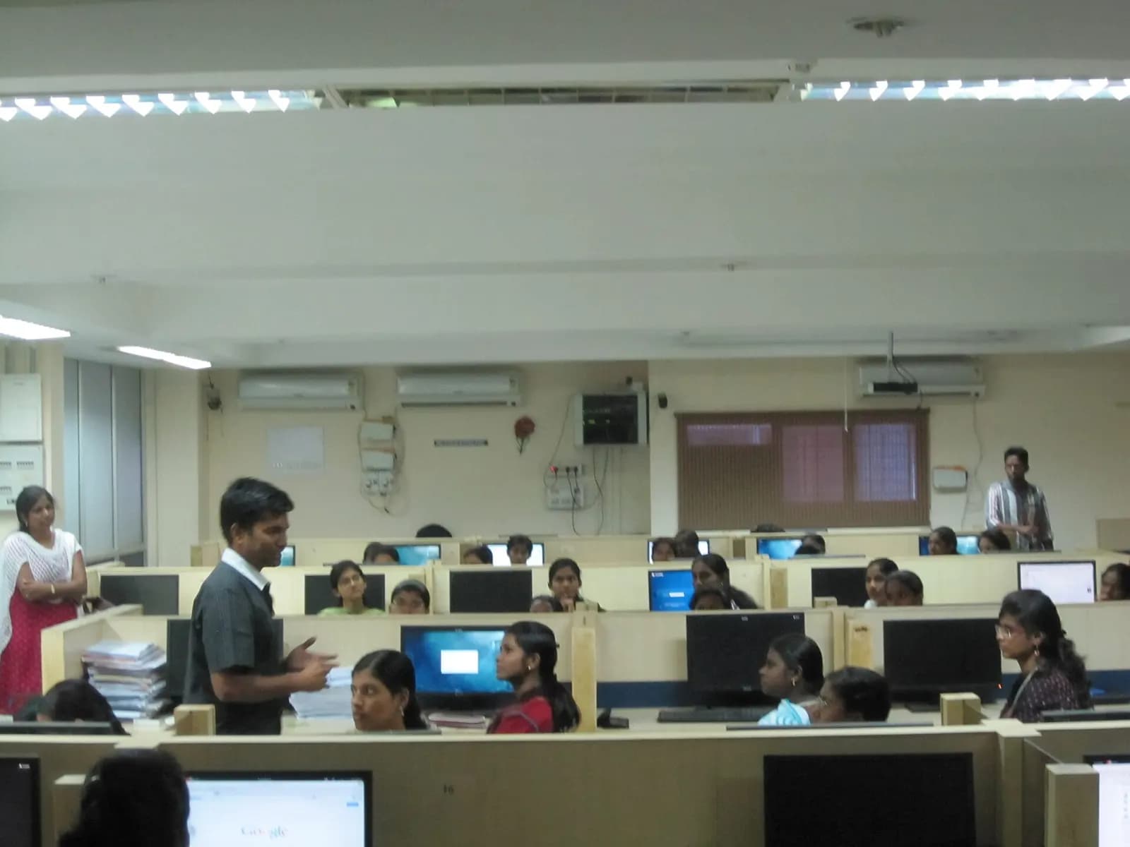Computer lab in an Indian college with students working at desktop computers and an instructor standing