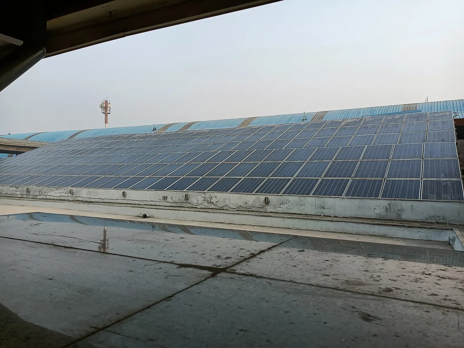Rows of solar panels mounted across a large flat roof in an Indian city under a hazy sky
