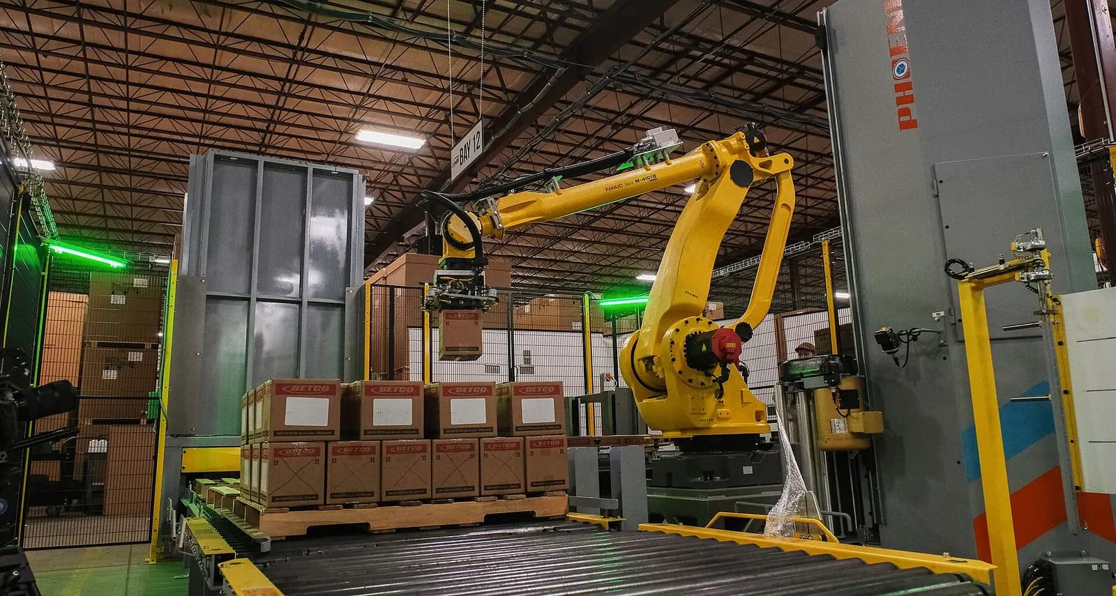 Yellow palletising robot stacking boxes onto a pallet at the end of a warehouse conveyor