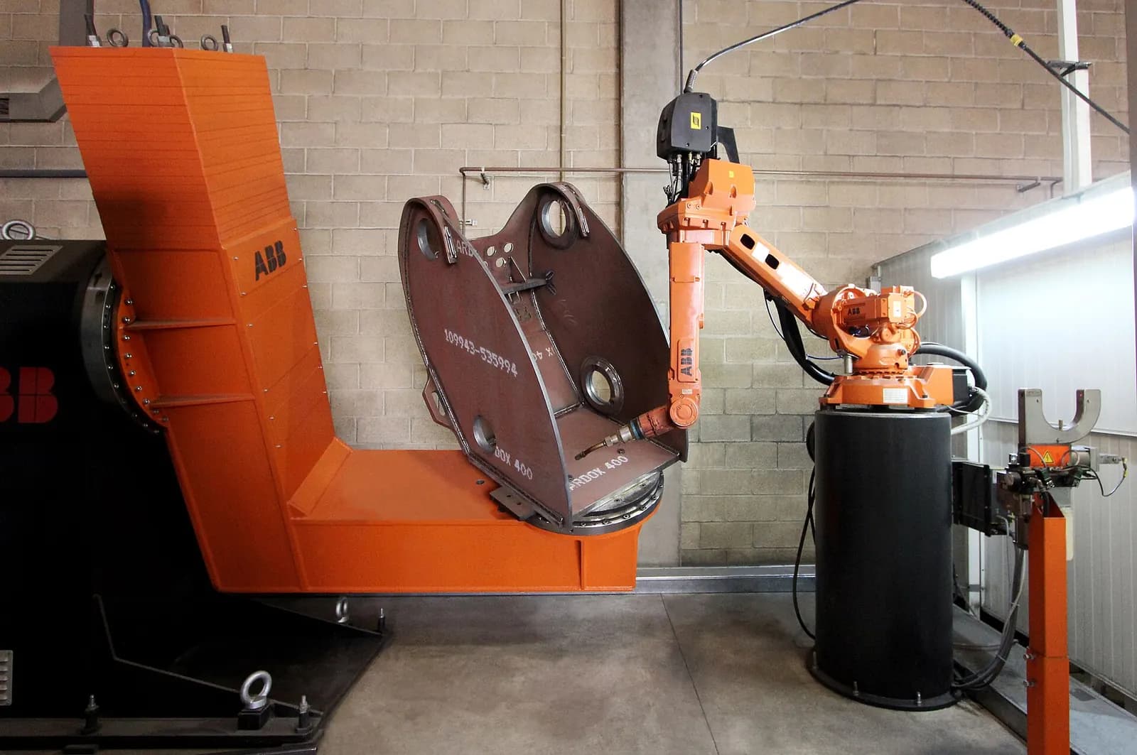 Orange six-axis welding robot beside a large two-station positioner inside a welding cell