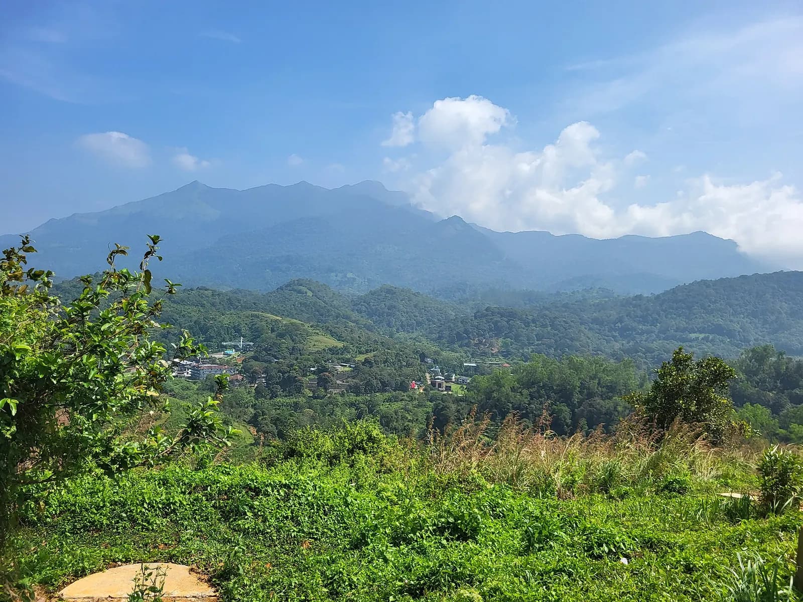 Green hills and forested valleys of Wayanad seen from a hilltop near Pookode under a blue sky with clouds