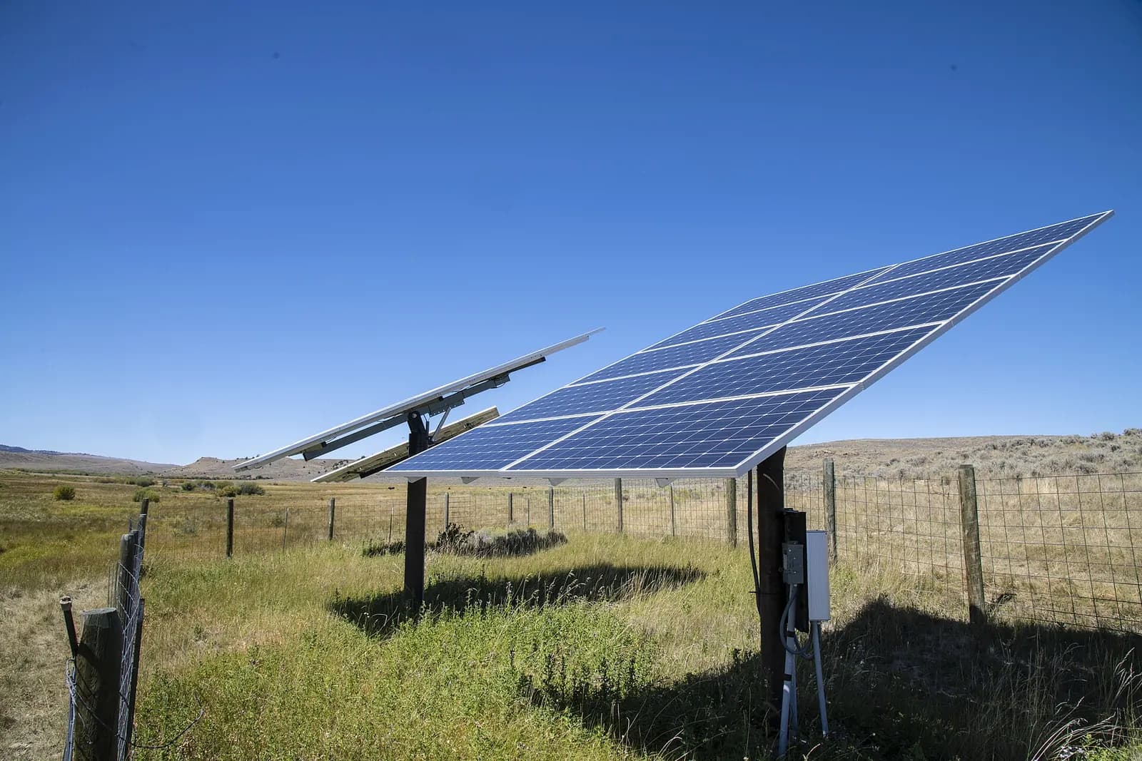 Tilted solar panel array on a steel frame powering a water pump in an open grassy field