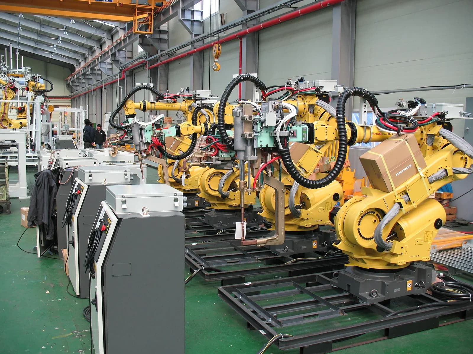 Several yellow industrial robots with spot welding guns installed on a factory floor before commissioning