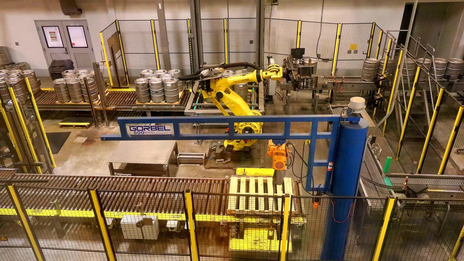Yellow industrial robot palletising cases inside a fenced cell at a brewery