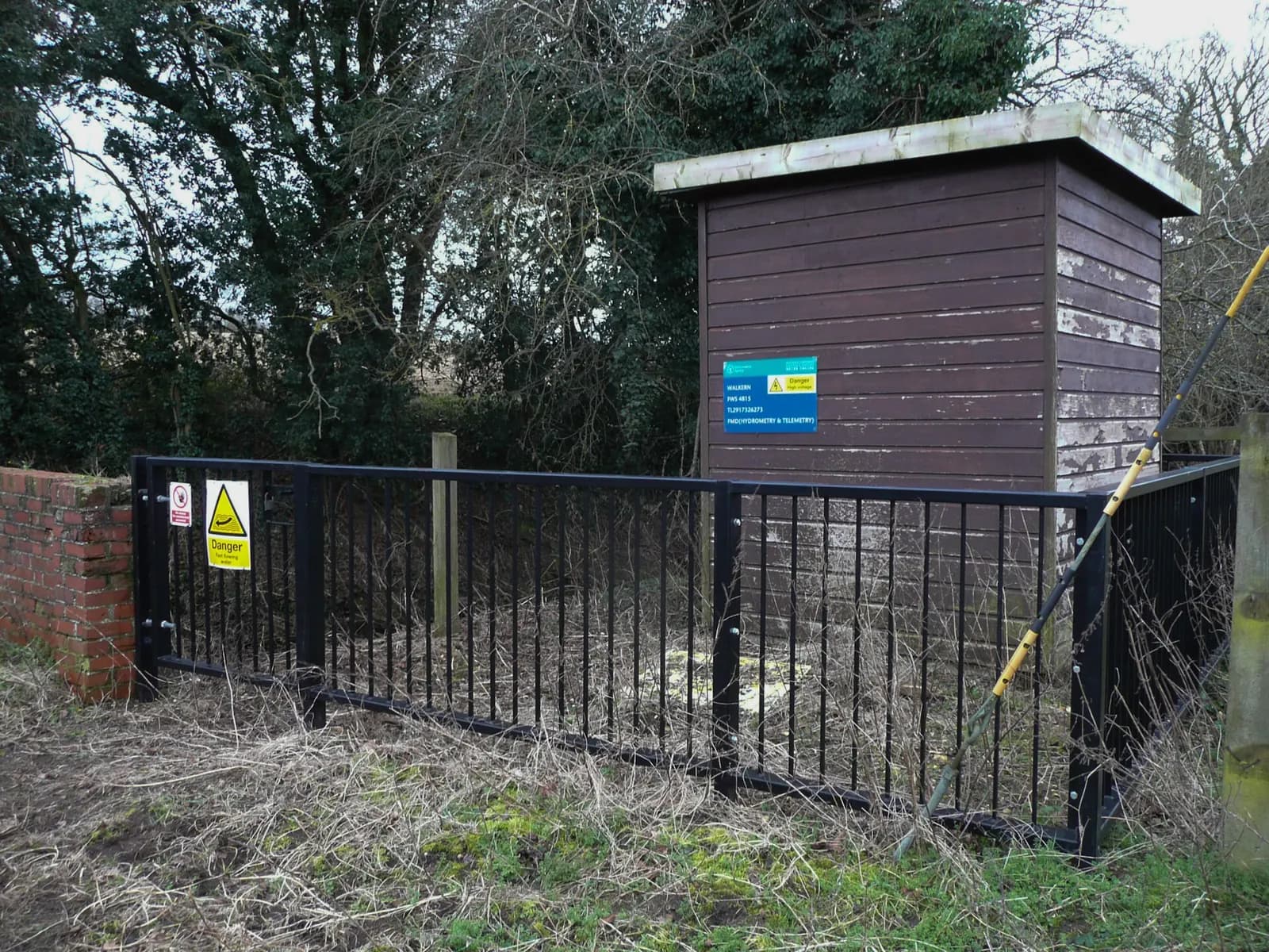 Wooden hydrometry and telemetry kiosk behind railings at Walkern, Hertfordshire