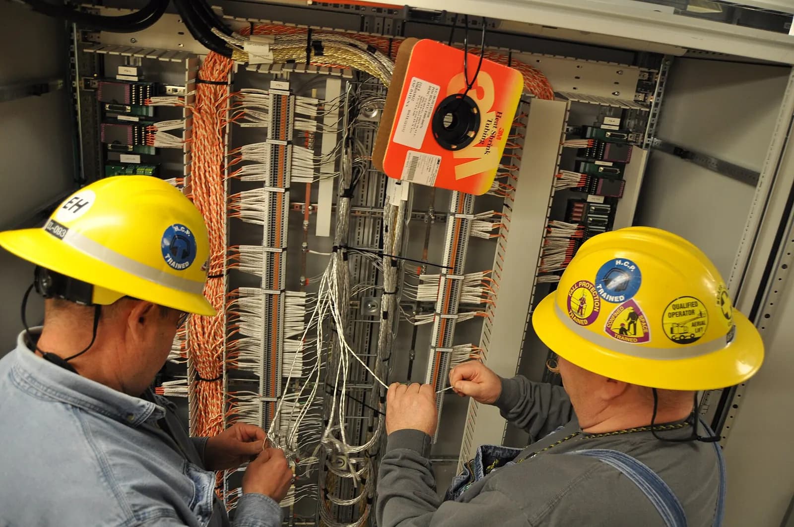 Two technicians in hard hats wiring terminal strips inside control cabinets