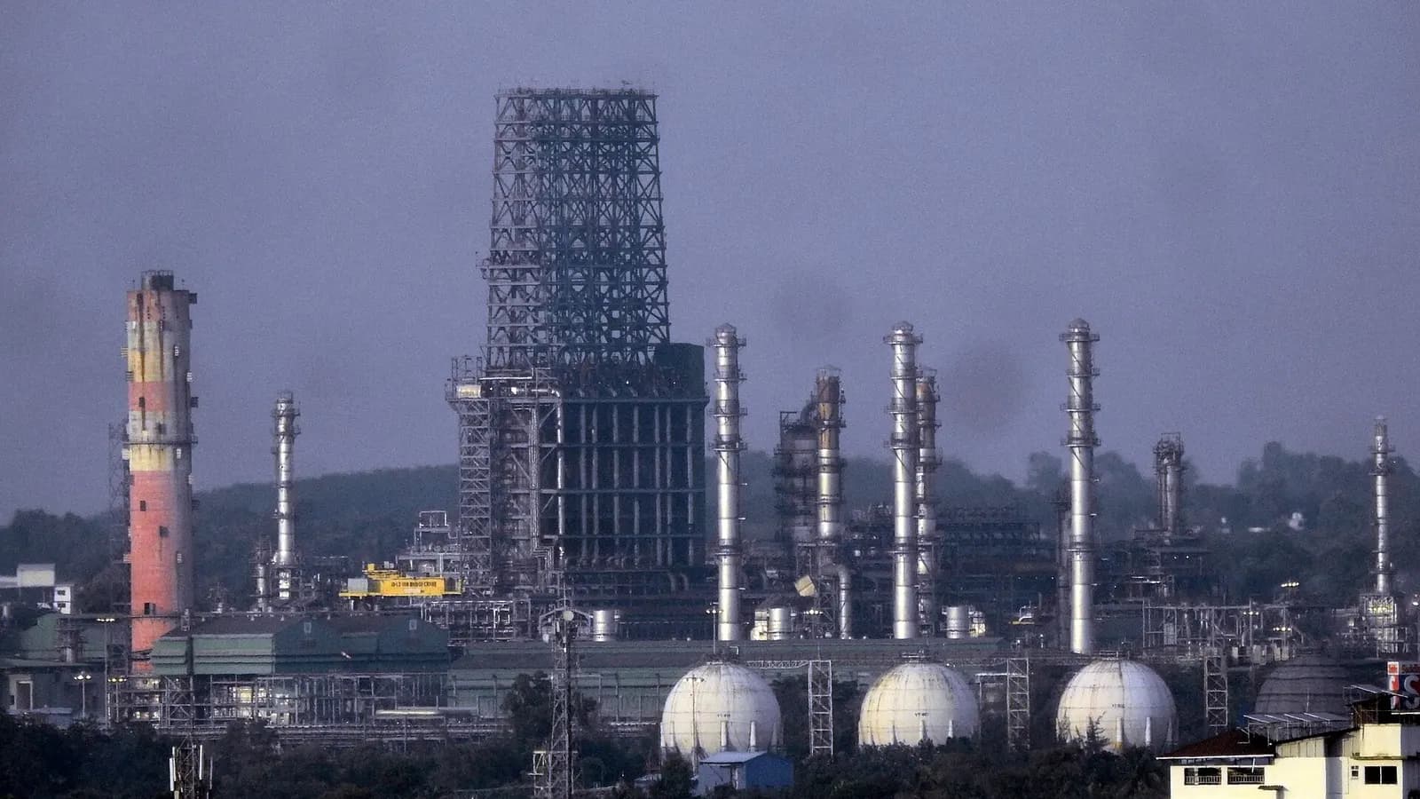 Distillation columns, flare stack and spherical storage tanks at the BPCL Kochi oil refinery under a cloudy sky.