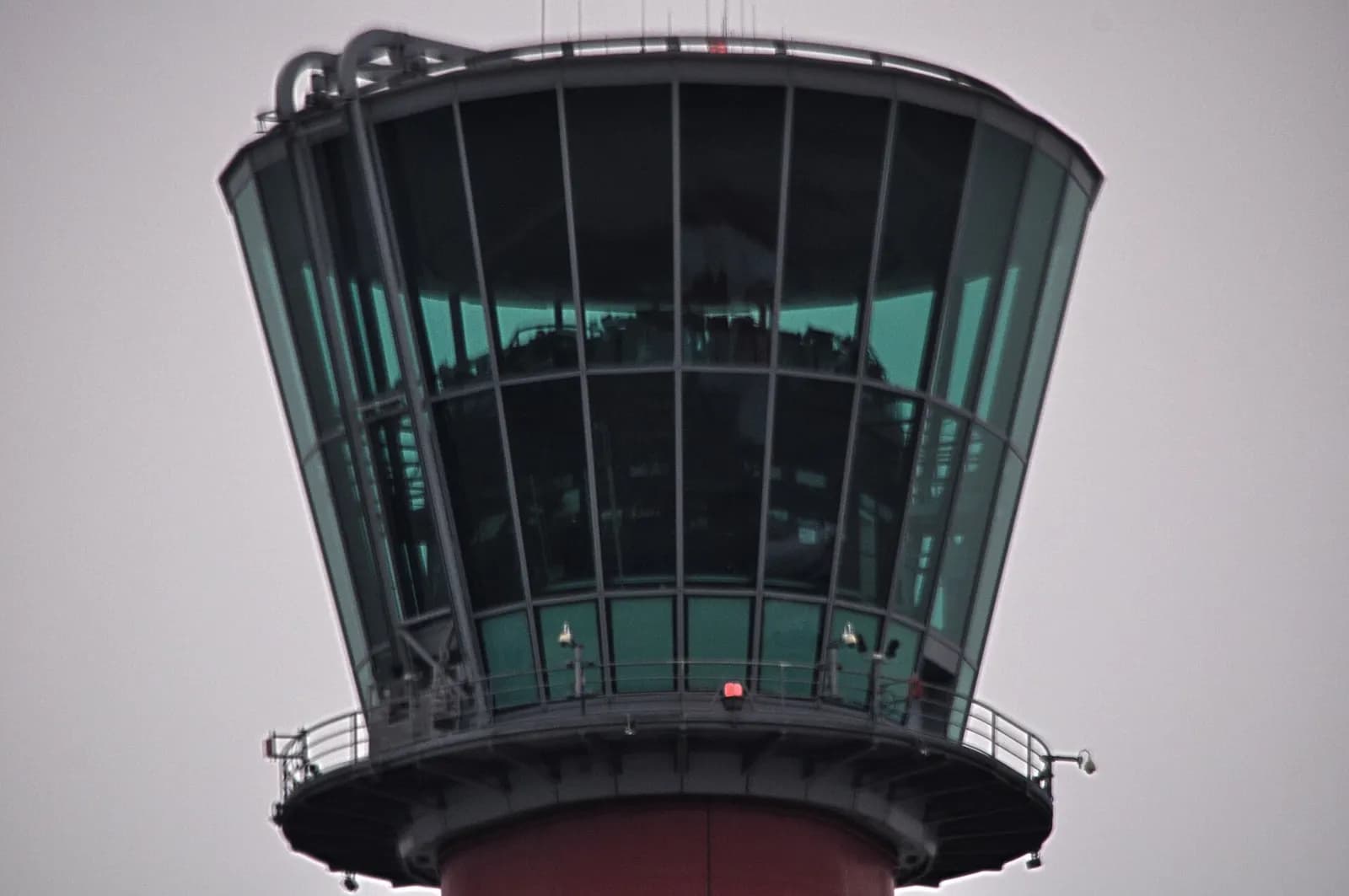 Close view of the glazed cab of the air traffic control tower at London Heathrow Airport against a grey sky.