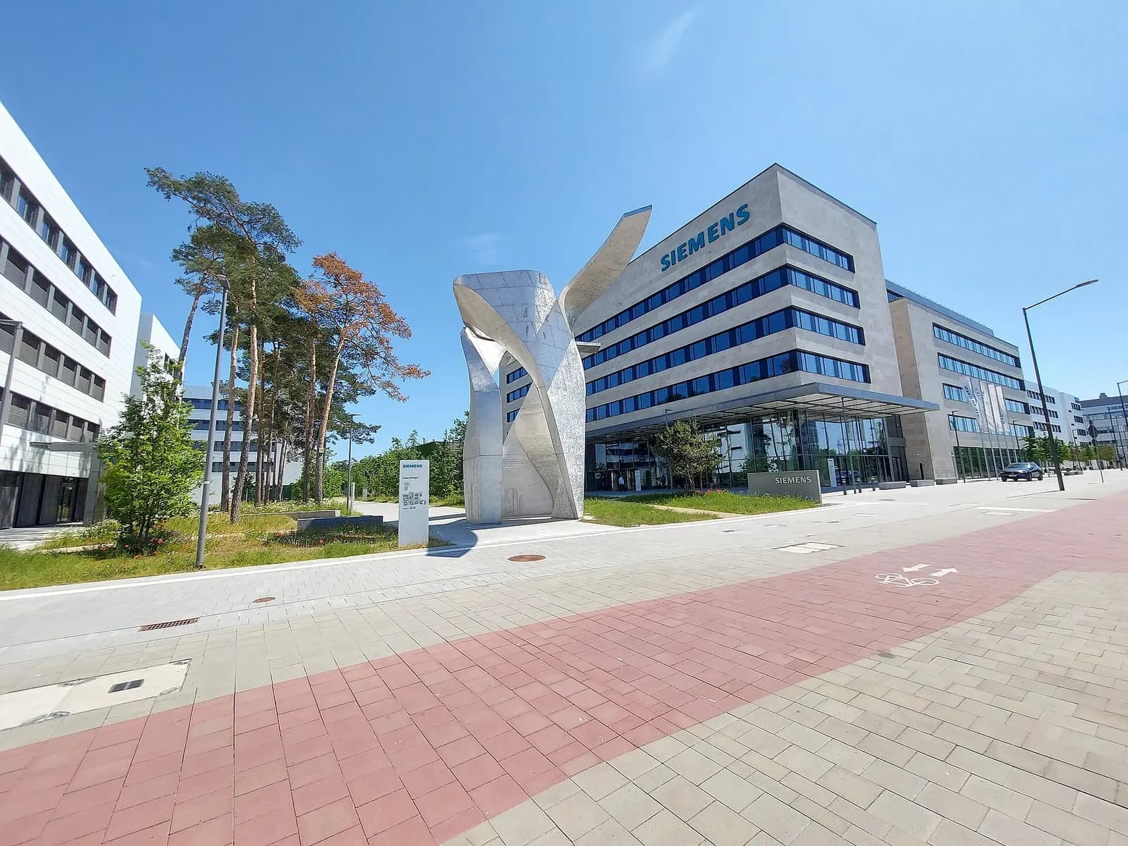 Modern office buildings of the Siemens Campus in Erlangen with a tall metal sculpture and a paved walkway.