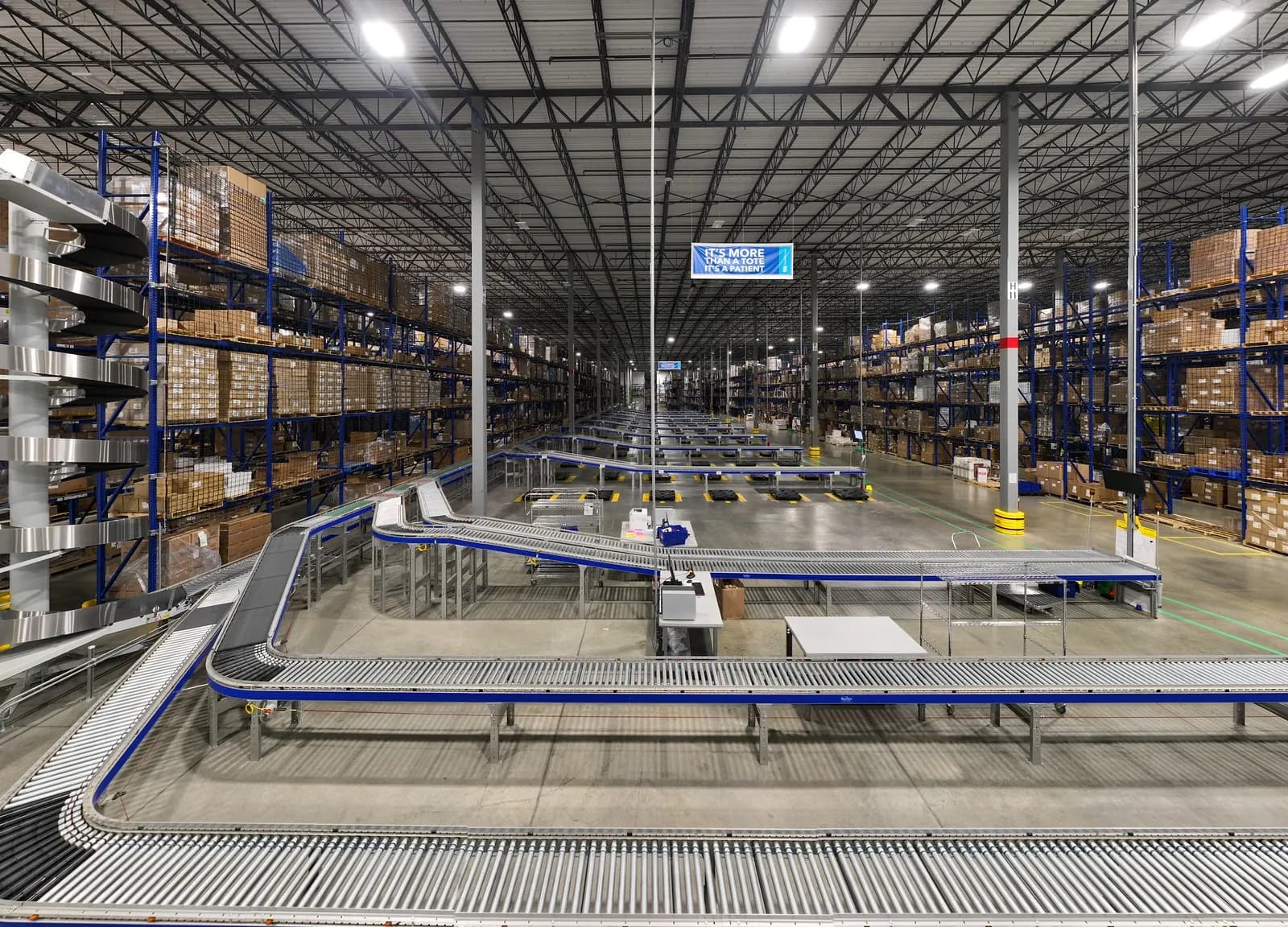 Interior of a large distribution centre with tall pallet racking and a powered roller conveyor sortation system.