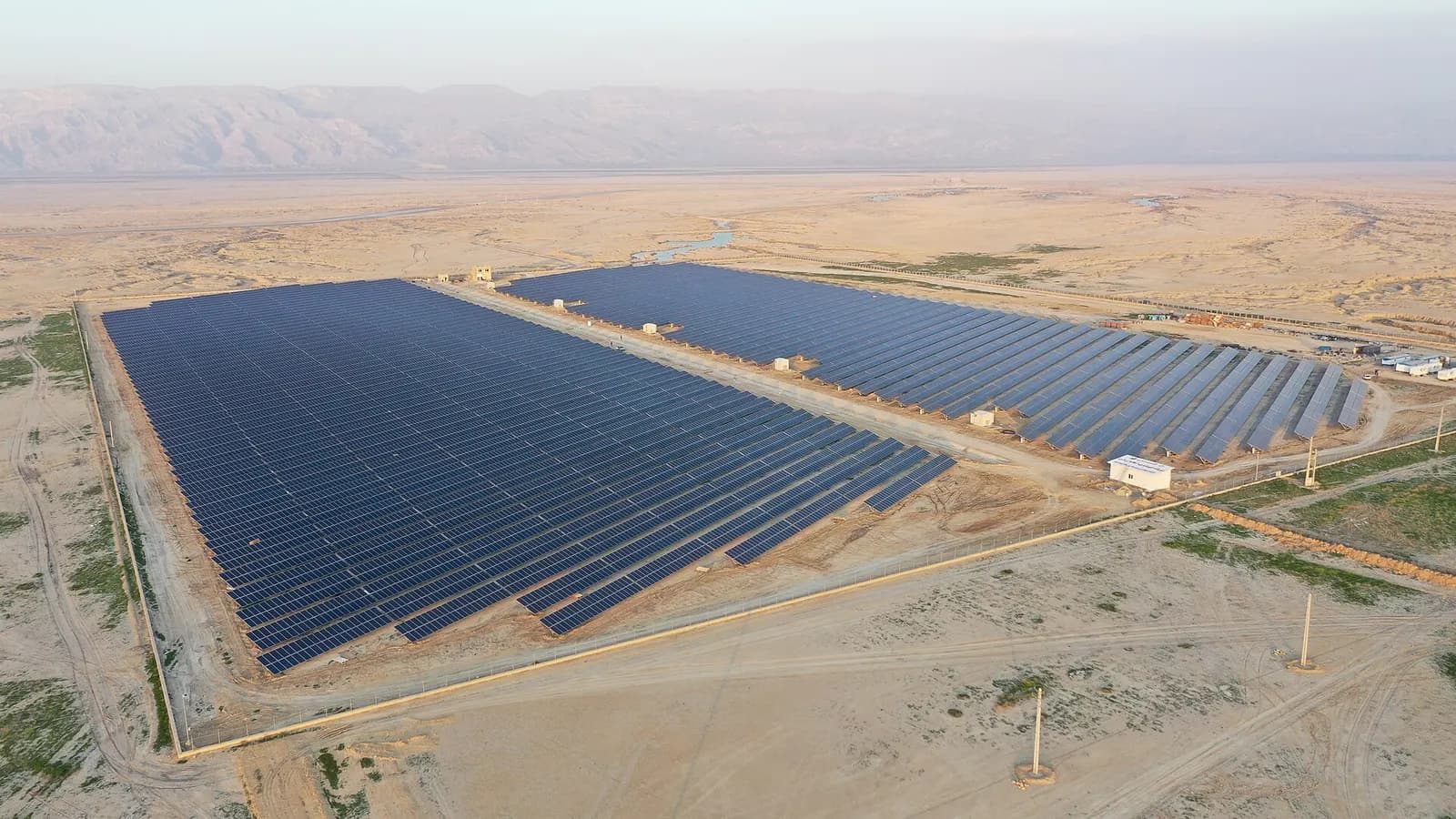 Aerial view of a utility-scale photovoltaic power station with long rows of solar panels in a desert landscape.